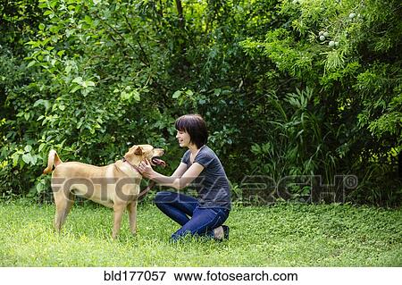 Stock Photo - Caucasian woman petting dog in field. Fotosearch