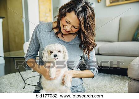 Stock Image - Caucasian woman petting dog in living room. Fotosearch