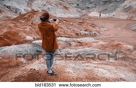 Stock Image - Caucasian woman photographing rock formations. Fotosearch