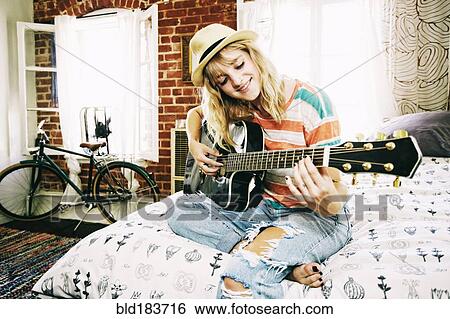 Stock Photograph - Caucasian woman playing guitar in bedroom. Fotosearch