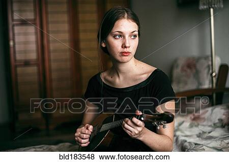 Stock Photo - Caucasian woman playing ukulele in bedroom. Fotosearch