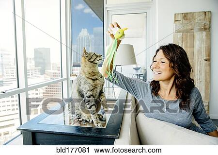 Stock Image - Caucasian woman playing with cat in living room. Fotosearch