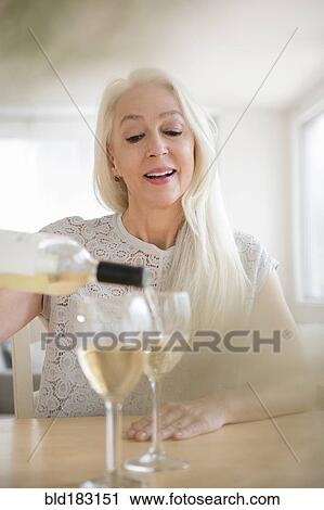 Stock Image - Caucasian woman pouring glasses of white wine. Fotosearch