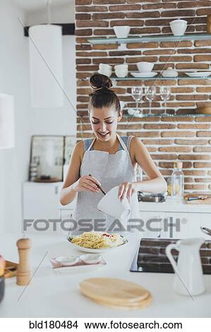 Picture - Caucasian woman pouring sauce on pasta in kitchen. Fotosearch