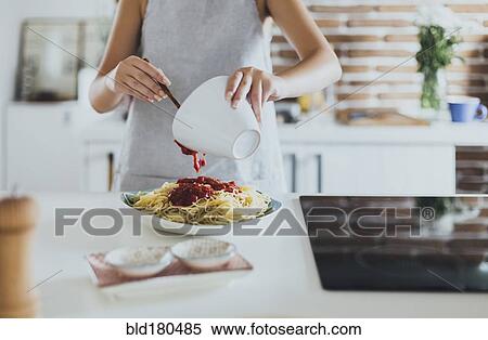 Stock Photography - Caucasian woman pouring sauce on pasta in kitchen. Fotosearch