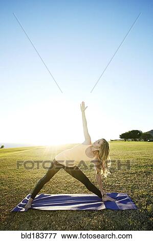 Stock Photo - Caucasian woman practicing yoga in field. Fotosearch