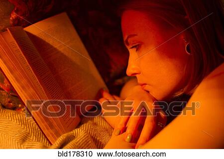 Stock Image - Caucasian woman reading book in bed. Fotosearch