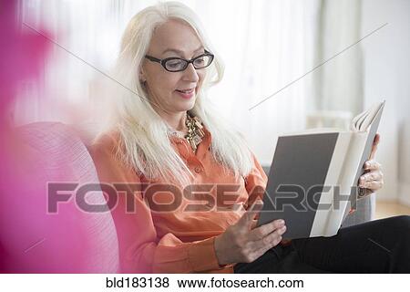 Stock Photo - Caucasian woman reading book on sofa. Fotosearch