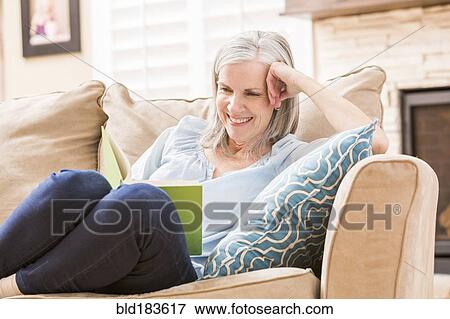 Stock Photo - Caucasian woman reading book on sofa. Fotosearch