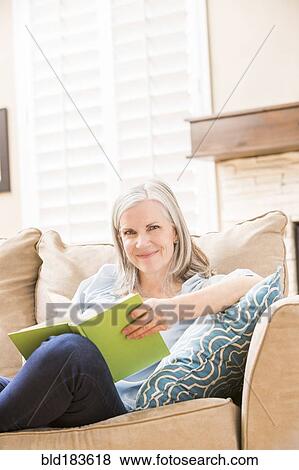 Stock Photo - Caucasian woman reading book on sofa. Fotosearch