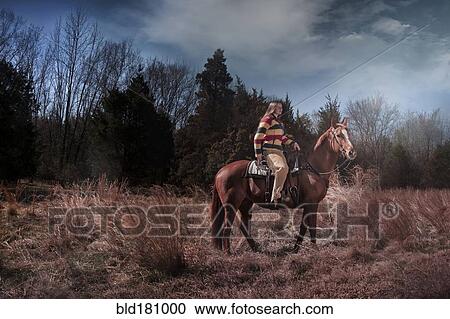 Stock Image - Caucasian woman riding horse in rural field. Fotosearch