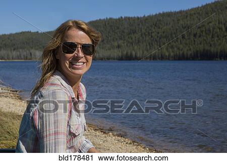 Stock Image - Caucasian woman sitting at remote lake. Fotosearch