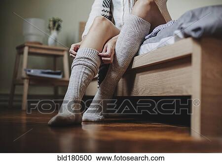 Stock Image - Caucasian woman sitting on bed pulling up socks. Fotosearch