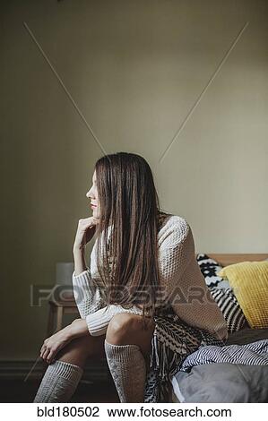 Stock Image - Caucasian woman sitting on bed. Fotosearch