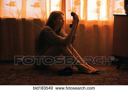 Stock Photo - Caucasian woman sitting on floor staring at telephone. Fotosearch