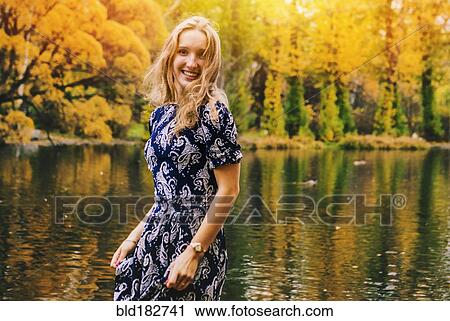 Stock Image - Caucasian woman smiling near pond in park. Fotosearch