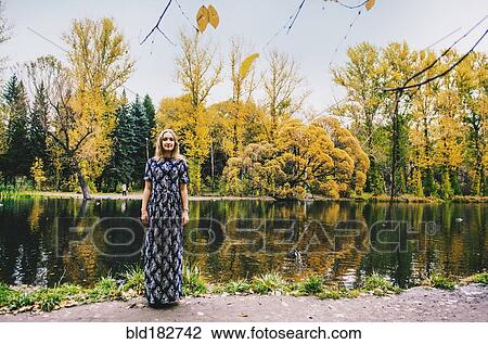 Stock Image - Caucasian woman smiling near pond in park. Fotosearch