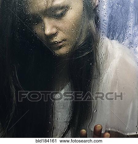 Stock Image - Caucasian woman standing at wet glass. Fotosearch