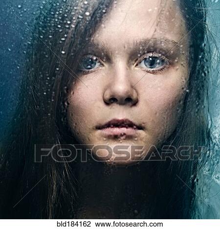 Stock Image - Caucasian woman standing at wet glass. Fotosearch
