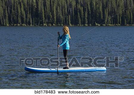 Stock Image - Caucasian woman standing on paddle board in river. Fotosearch