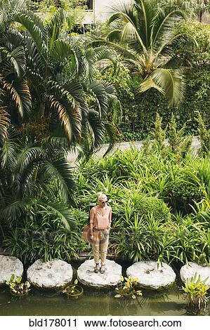 Stock Image - Caucasian woman standing on stone in pond. Fotosearch
