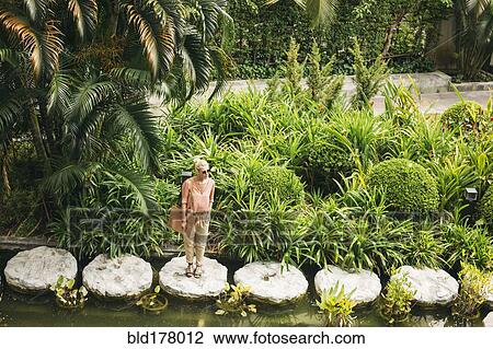 Stock Image - Caucasian woman standing on stone in pond. Fotosearch