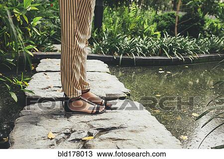 Stock Image - Caucasian woman standing on stone in pond. Fotosearch