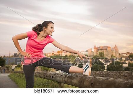 Stock Image - Caucasian woman stretching leg outdoors. Fotosearch