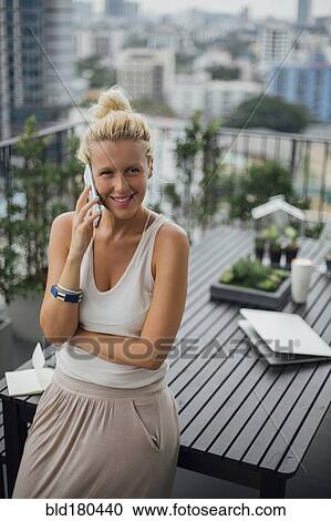 Stock Image - Caucasian woman talking on cell phone on balcony. Fotosearch