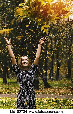 Picture - Caucasian woman tossing autumn leaves in park. Fotosearch