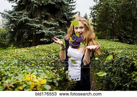 Stock Image - Caucasian woman tossing leaves in garden. Fotosearch