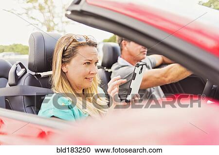 Stock Image - Caucasian woman using cell phone in convertible. Fotosearch