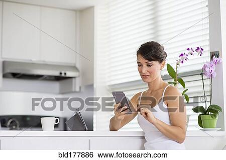 Caucasian woman using cell phone in kitchen View Large Photo Image Stock Photograph - Caucasian woman using cell phone in kitchen. Fotosearch