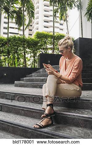 Stock Image - Caucasian woman using cell phone on stairs. Fotosearch