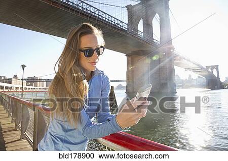 Stock Image - "Caucasian woman using cell phone on waterfront, New York, New York, United States". Fotosearch