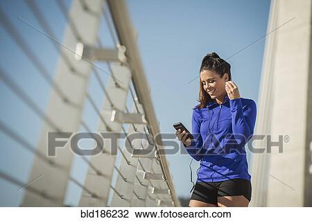 Stock Image - Caucasian woman using cell phone on urban bridge. Fotosearch
