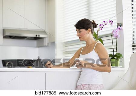 Stock Photography - Caucasian woman using digital tablet in kitchen. Fotosearch