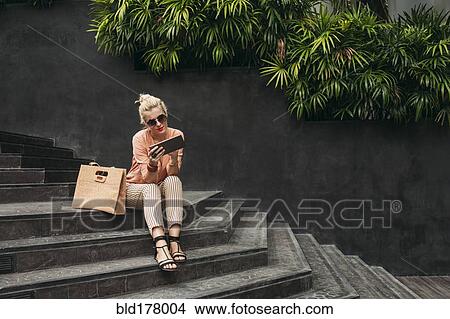 Picture - Caucasian woman using digital tablet on stairs. Fotosearch