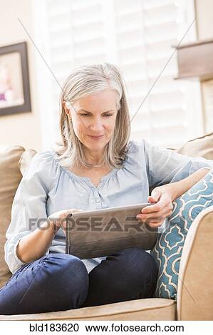 Stock Image - Caucasian woman using digital tablet on sofa. Fotosearch