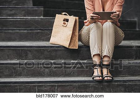 Stock Photo - Caucasian woman using digital tablet on stairs. Fotosearch