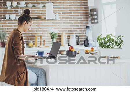 Picture - Caucasian woman using laptop in kitchen. Fotosearch