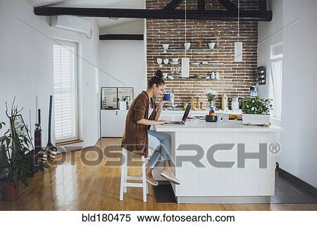 Stock Photography - Caucasian woman using laptop in kitchen. Fotosearch