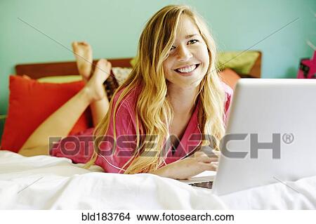 Picture - Caucasian woman using laptop on bed. Fotosearch