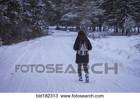 Stock Image - Caucasian woman walking on snowy rural road. Fotosearch