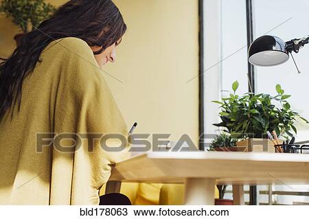 Stock Image - Caucasian woman writing at desk. Fotosearch