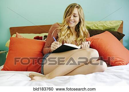 Stock Image - Caucasian woman writing in diary on bed. Fotosearch