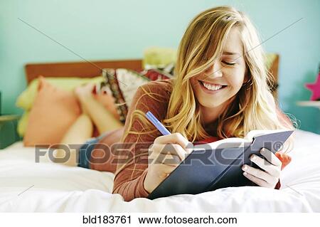 Stock Image - Caucasian woman writing in diary on bed. Fotosearch