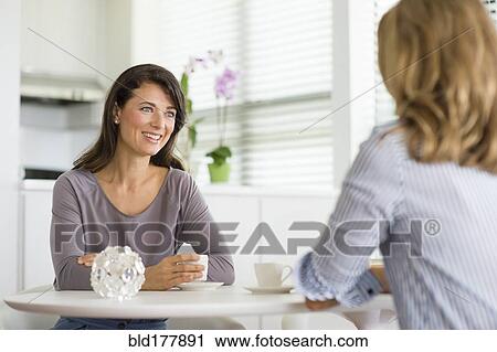 Stock Image - Caucasian women drinking coffee in kitchen. Fotosearch