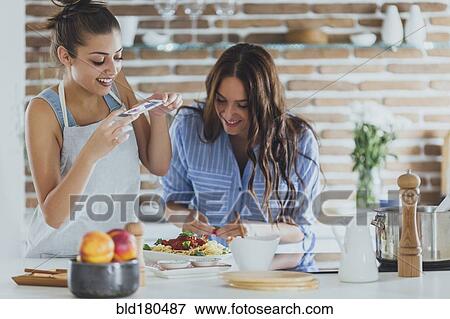 Stock Photo - Caucasian women photographing pasta in kitchen. Fotosearch