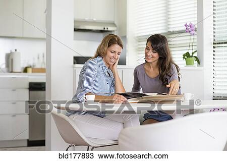 Stock Image - Caucasian women reading magazine in kitchen. Fotosearch